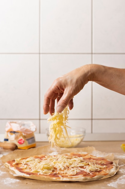 Hand die mozarella op pizzadeeg bestrooit