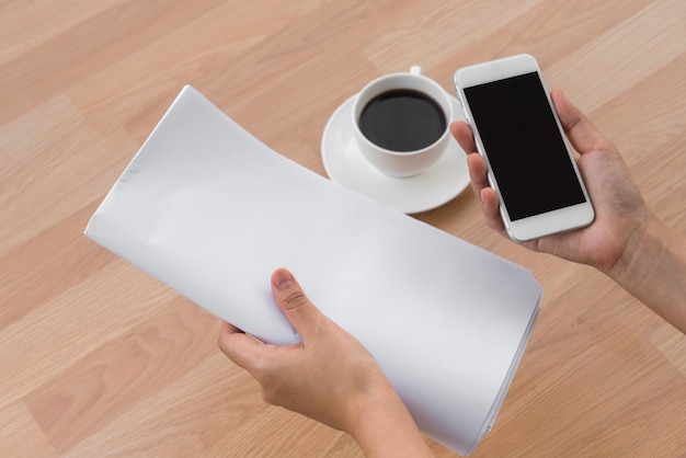 Hand houden van een vel papier, een mobiele telefoon en een kopje koffie op de tafel