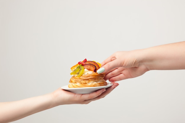 Hand met cake met vers fruit op grijs