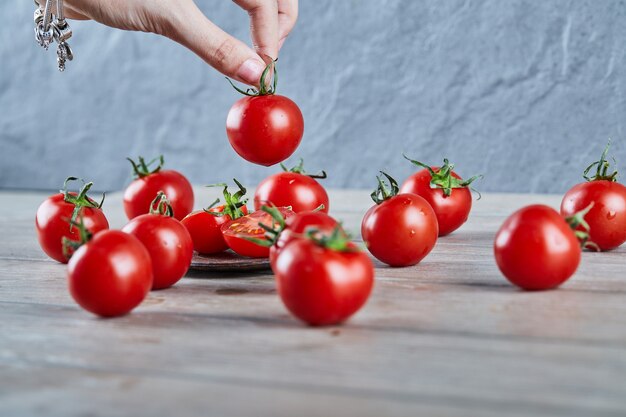 Hand met een tomaat met een bos tomaten op houten tafel