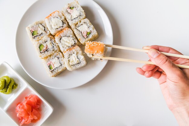 Hand met eetstokjes die een sushibroodje grijpen