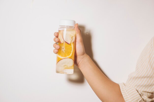 Hand met fles water met sinaasappel en appel op lichte achtergrond