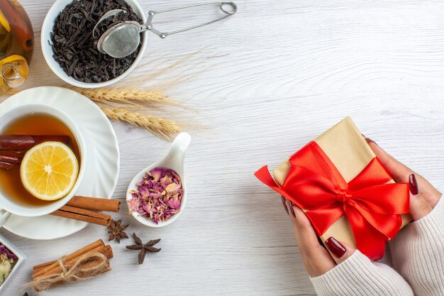 Hand met geschenken met rood lint en theepauze met kaneel