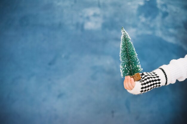 Hand met kleine kerstboom en ruimte aan de linkerkant