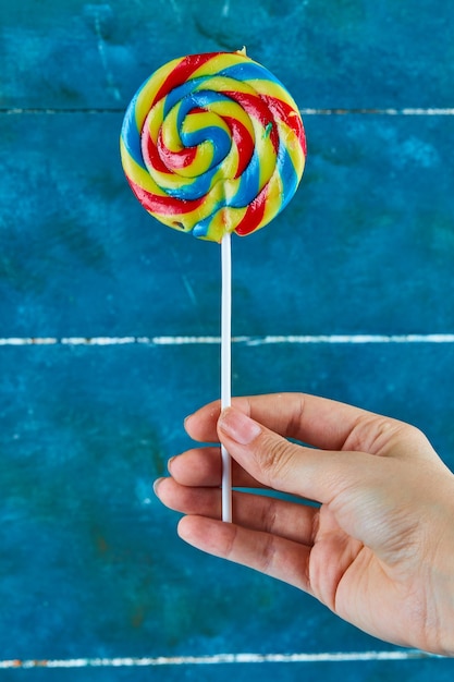 Hand met kleurrijke lolly op blauwe ondergrond.