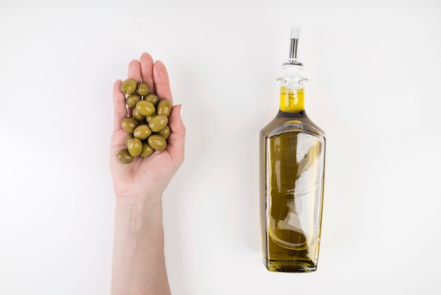 Hand met olijven naast fles olie