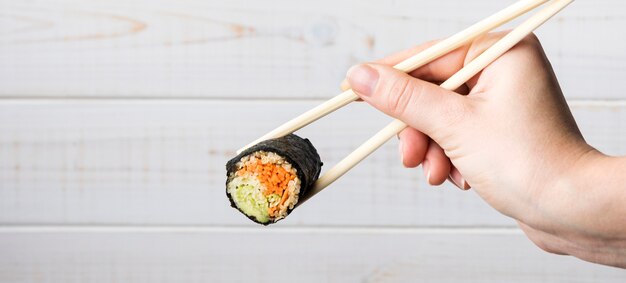 Hand met stokjes en sushi roll