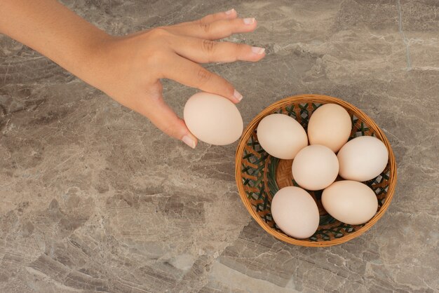 Hand nemen van een ei en een mand met witte eieren.