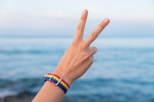 Hand van een persoon in een kleurrijke armband die het V-teken gebaart