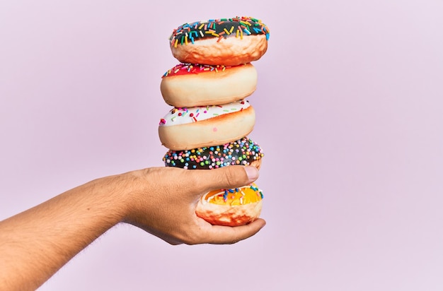 Gratis foto hand van een spaanse man die een toren van donuts vasthoudt op een geïsoleerde roze achtergrond