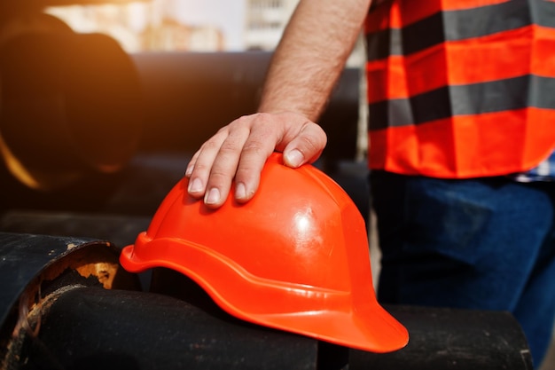 Hand van werknemer man in oranje veiligheidshelm in de buurt van stalen buizen