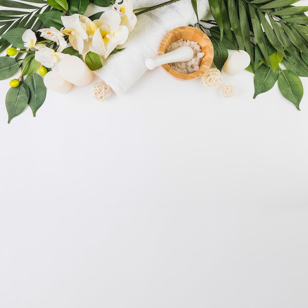 Handdoek; zout; kaarsen; bloemen en bladeren op wit oppervlak