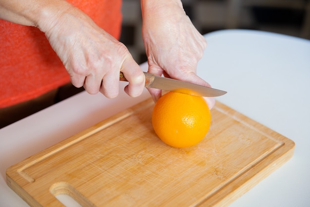 Handen die sinaasappel houden en het met mes snijden