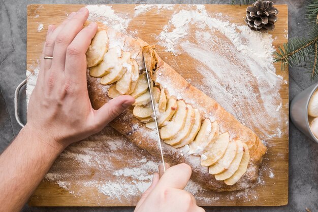 Handen die smakelijke cake op hakbord snijden