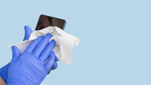 Handen met chirurgische handschoenen die smartphone met exemplaarruimte desinfecteren