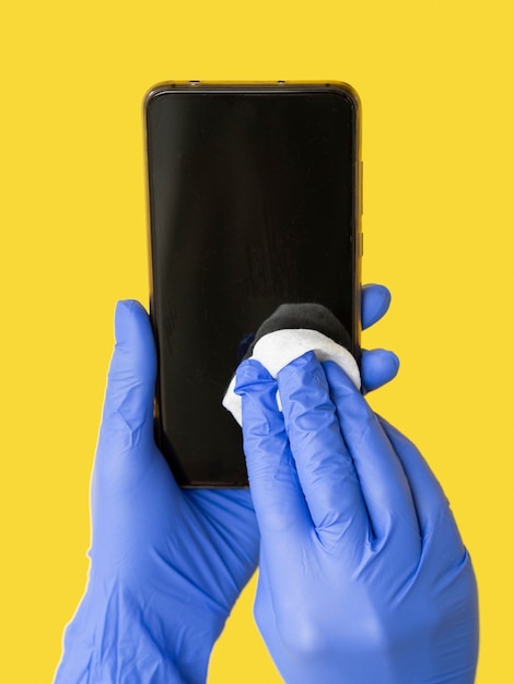 Handen met chirurgische handschoenen die smartphone met servet desinfecteren