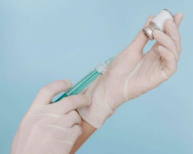 Handen met handschoenen die een spuit met vaccinfles houden