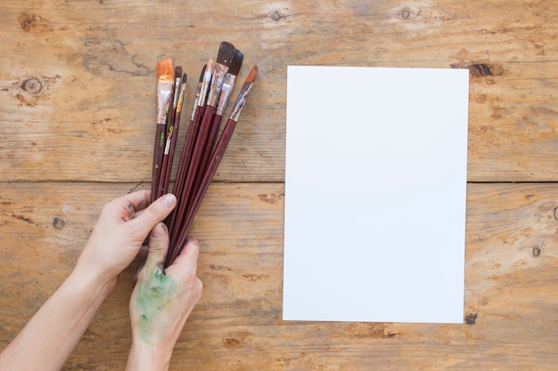 Gratis foto handen met penselen in de buurt van witboek