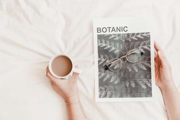 Handen met warme drank en poster met bril op bedsheet
