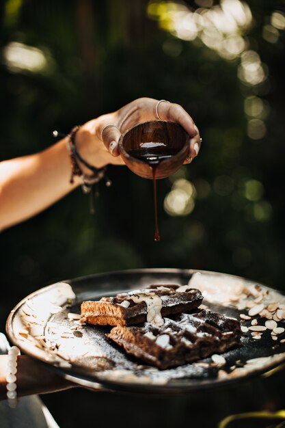 Handen met zwarte plaat met wafels, pinda's en chocoladesaus