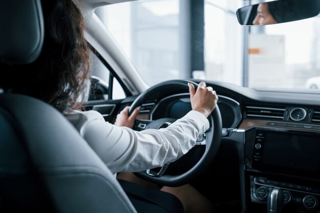 Handen op het stuur. Mooie zakenvrouw probeert haar nieuwe auto in de auto salon