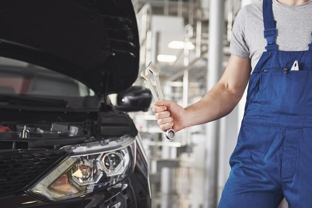 Handen van automonteur met moersleutel in garage.