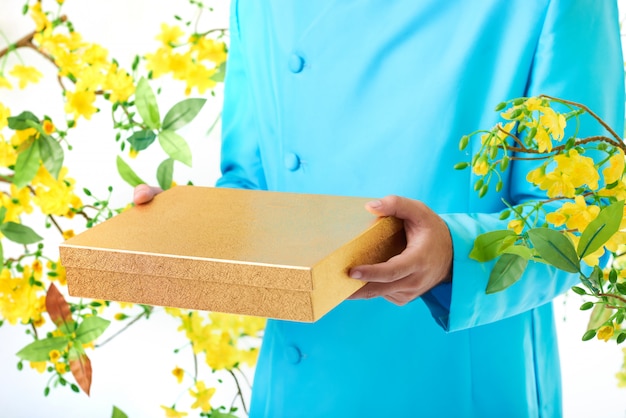 Gratis foto handen van de onherkenbare man in traditionele jas poseren met bloeiende mimosa en vierkante doos