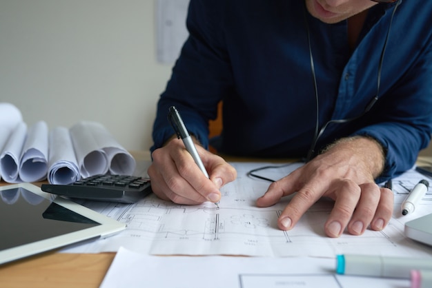 Handen van de onherkenbare mens die op technisch plan in bureau trekken