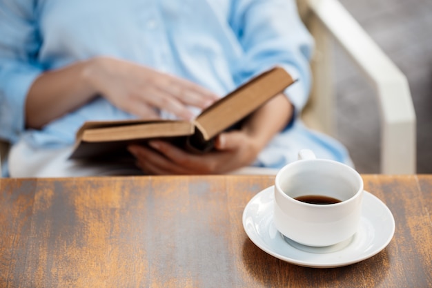 Handen van een jong meisje zitten aan de tafel met boek en koffiekopje.