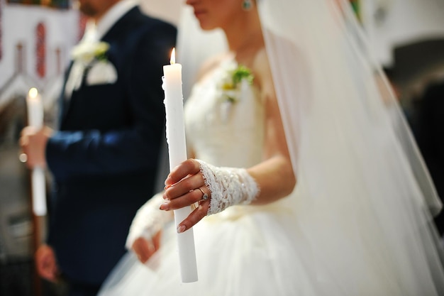 Handen van jonggehuwde met kaars in kerk