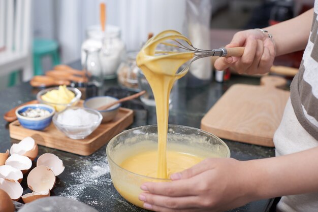 Handen van onherkenbaar vrouw die beslag in kom in keuken thuis zwaaien