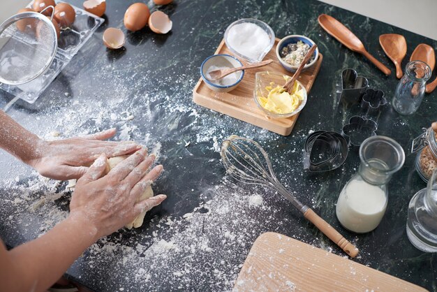 Handen van onherkenbaar vrouwen het kneden deeg op keukenteller thuis