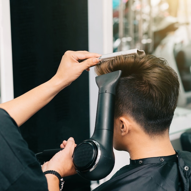 Handen van onherkenbare kapper die mannelijke klant blowdry met haardroger en kam geeft