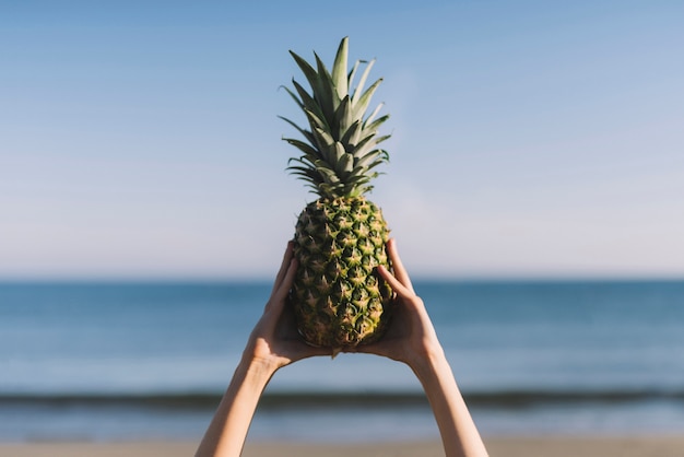 Handen verhogen ananas op het strand