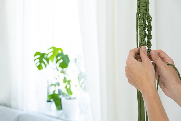 Handgemaakte groene macramé plantenhangers met potplant hangen aan de hand van de vrouw. in de macramé zit een pot en een monsteraplant.