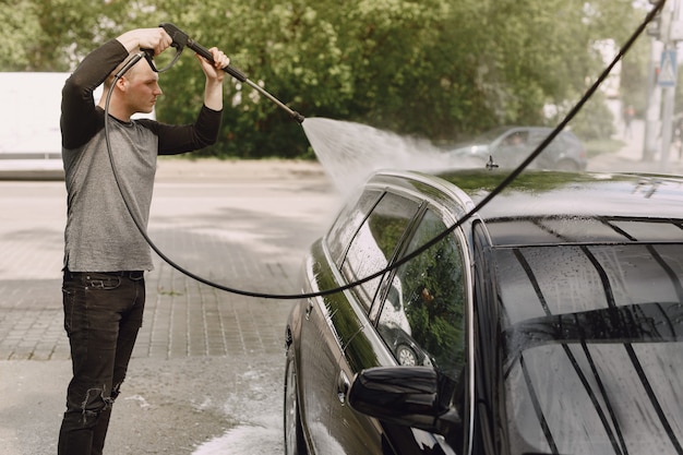 Handsomenmens in een zwarte sweater die zijn auto wassen