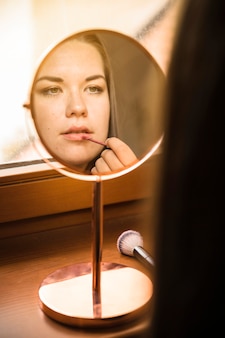 Handspiegel met weerspiegeling van vrouw die lippenstift op haar lippen toepast