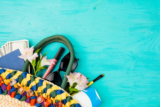 Gratis foto handtas met geld tussen bloemen in de buurt van zonnebril en lippenstift