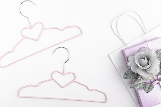 Hangers voor kleding en een geschenkdoos met een strik en witte verpakking op een lichtpaarse achtergrond. het concept van winkelen, kleding kopen, kortingen, verkoop, stylist.