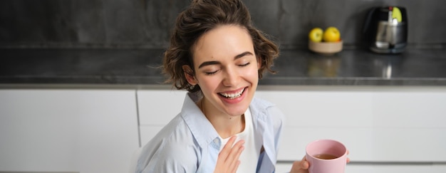 Gratis foto happy mornings portret van gelukkige brunette vrouw drinkt een kop koffie in haar keuken en glimlachend gezellig