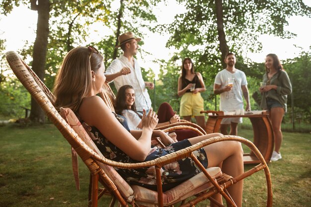 Happy vrienden eten en drinken van bier bij barbecue diner op zonsondergang tijd