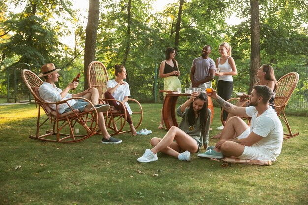 Happy vrienden eten en drinken van bier bij barbecue diner op zonsondergang tijd