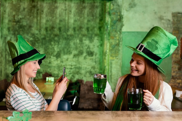 Happy vriendinnen vieren st. patrick's day samen met drankjes en smartphone