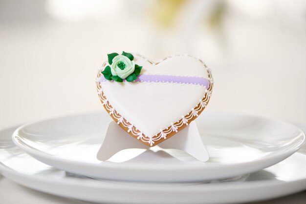 Hartvormig geglazuurd koekje - versierd met groene glazuurbloem en minuscule patroonstandaards op witte borden als decoratie voor een feestelijke bruiloftstafel. Op het witte restaurant staat een koekje