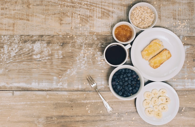 Haver; jam; koffie; bosbessen; banaan slice en toast op houten plank