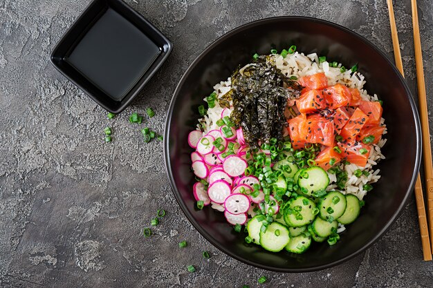 Hawaiiaanse zalm fish poke bowl met rijst, radijs, komkommer, tomaat, sesamzaad en zeewier. Boeddha schaal. Diëet voeding. Bovenaanzicht. Plat liggen.