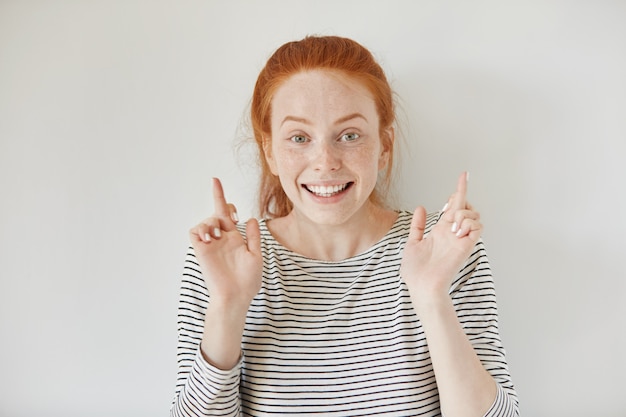 Gratis foto headshot van bijgelovig roodharige meisje houdt haar vingers gekruist, doet wensen en gelooft oprecht in haar succes of overwinning. mooie jonge vrouw met sproeten in de hoop dat haar dromen uitkomen