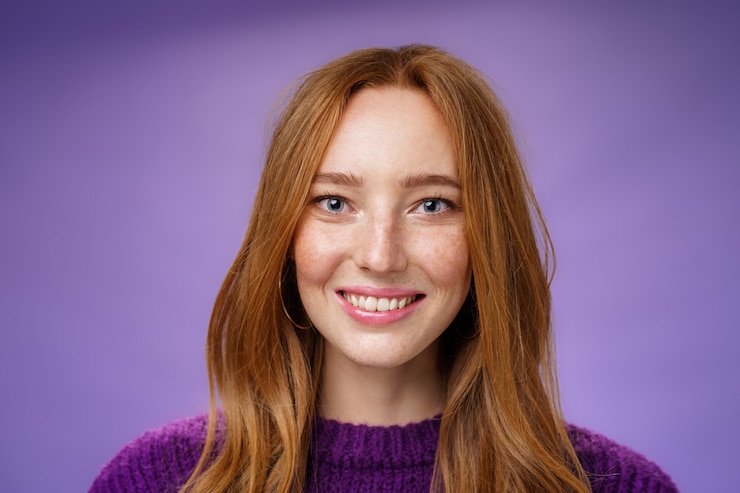 Gratis Foto headshot van charmante aantrekkelijke en gelukkige jonge roodharige vrouw met sproeten en heldere witte glimlach, tevreden grijnzend naar de camera als poseren over paarse achtergrond vriendelijk en opgetogen.