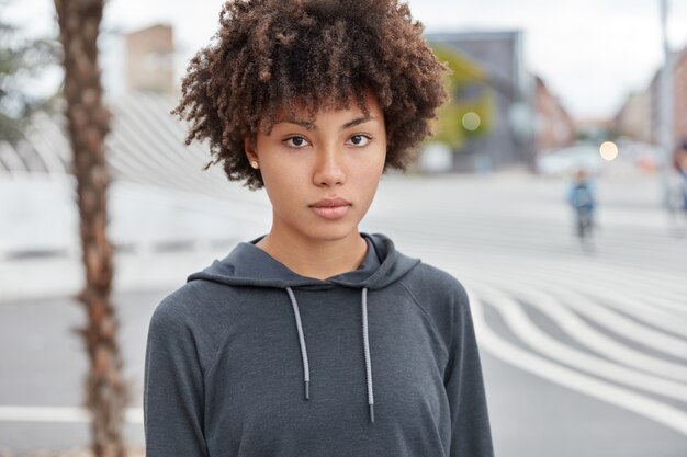 Headshot van ernstige doordachte vrouwelijke tiener gekleed in casual sweatshirt, gaat voor sport op straat