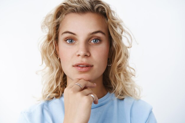Headshot van geïnteresseerde en gefocuste knappe creatieve jonge vrouw met kort krullend blond haar en blauwe ogen openen de lippen een beetje terwijl ze nieuwsgierig staren